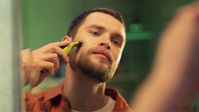 Tył głowy ciemnowłosego mężczyzny, kt&oacute;ry zbliża elektryczną golarkę do swojego policzka.