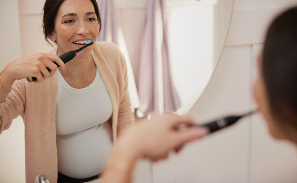 Kobieta w ciąży myje zęby szczoteczką elektryczną