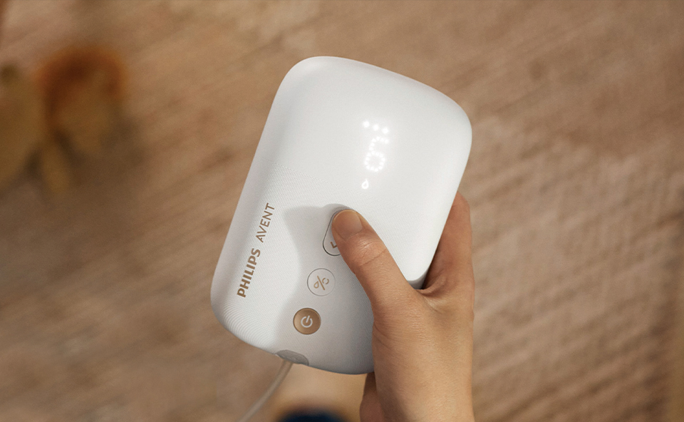 Ręka trzyma biały, elektryczny laktator marki Philips Avent